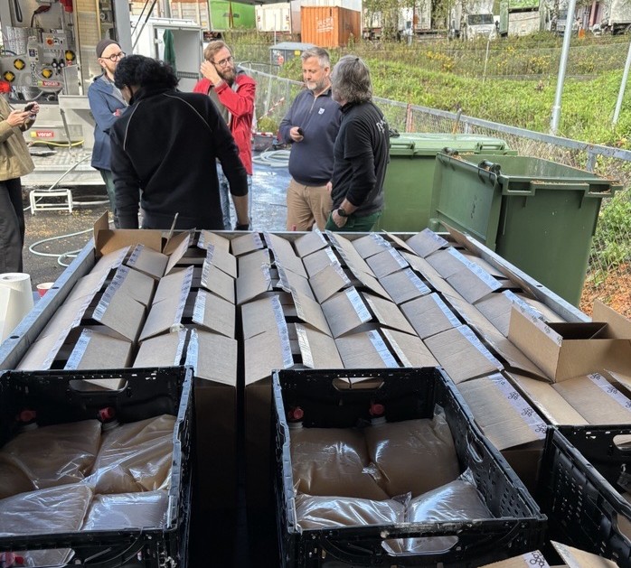 en henger med eplemost med fem mennesker stående bak som prater.