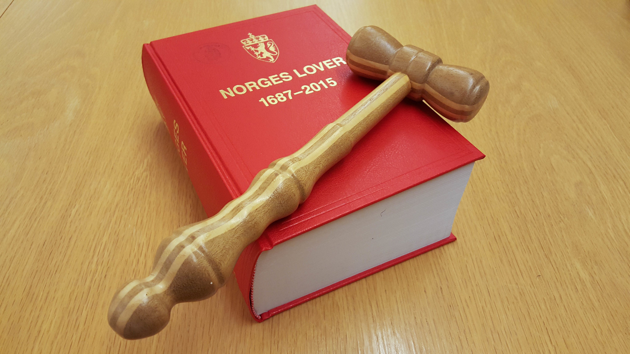 Bilde av norges lover, den røde boka med en dommerklubbe oppå. 