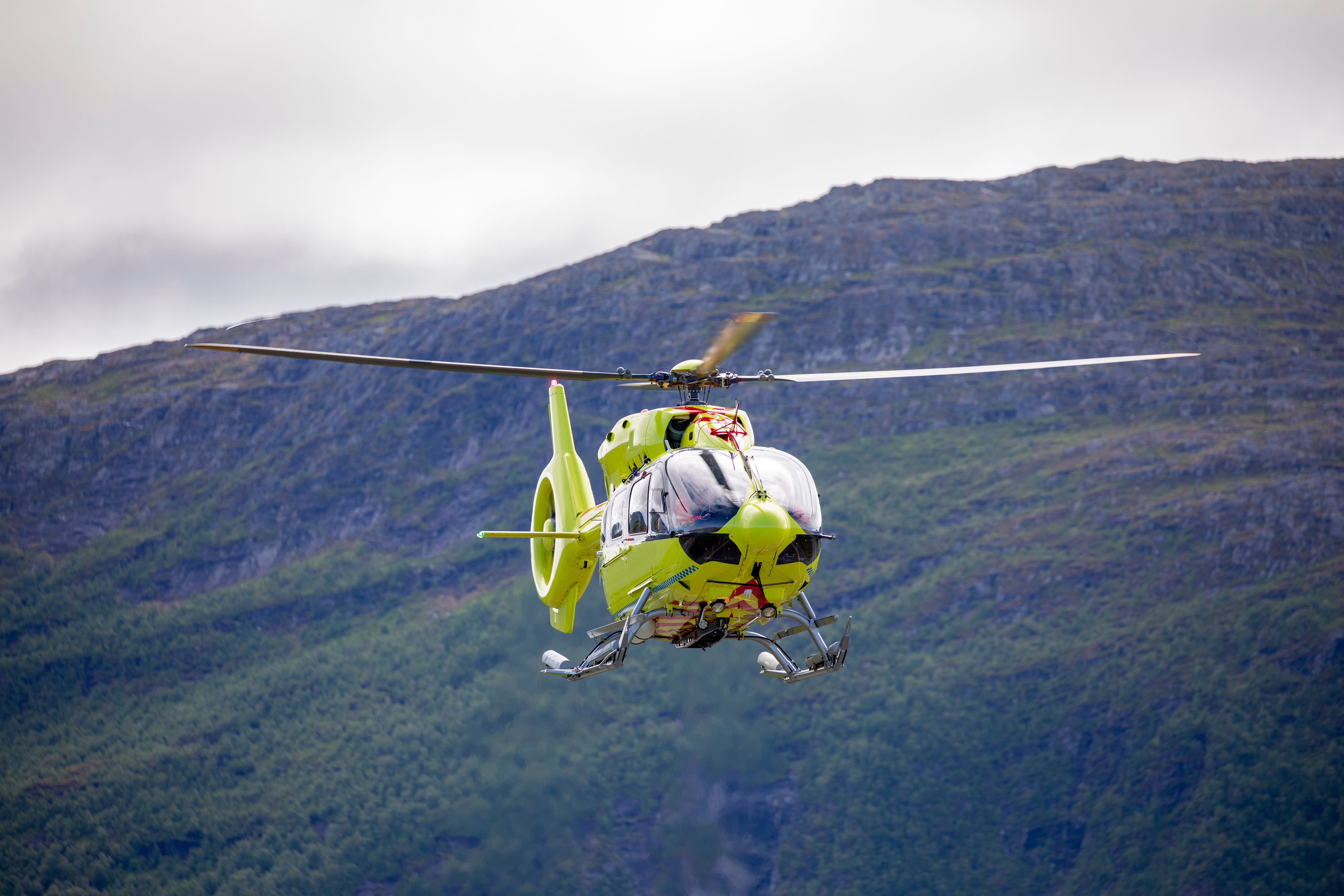 Gult luftambulanse helikopter som flyr foran et fjell