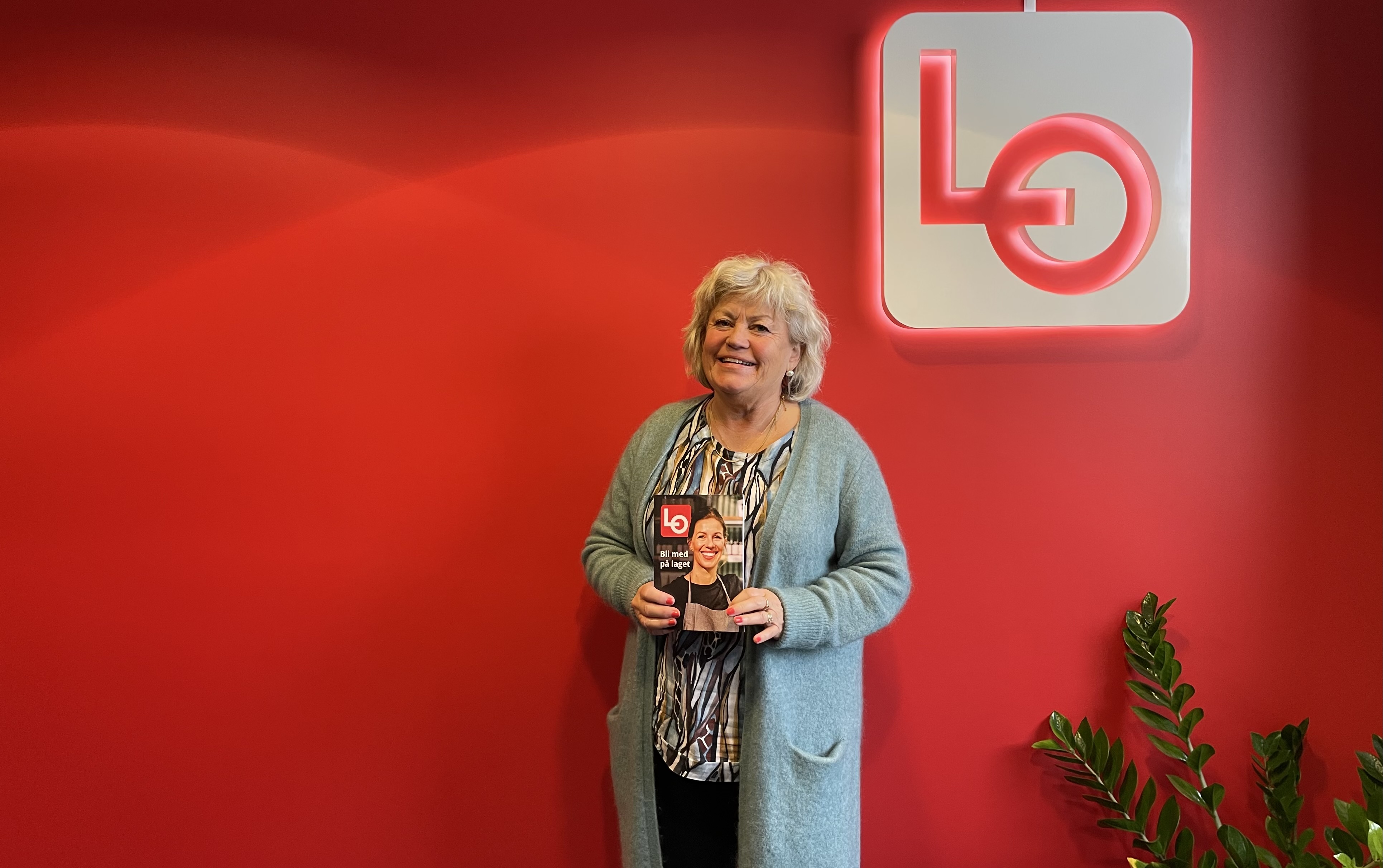 Heidi Elise Eikeland, Prosjektmedarbeider LOs serviceprosjekt forran rød vegg med lo-logo