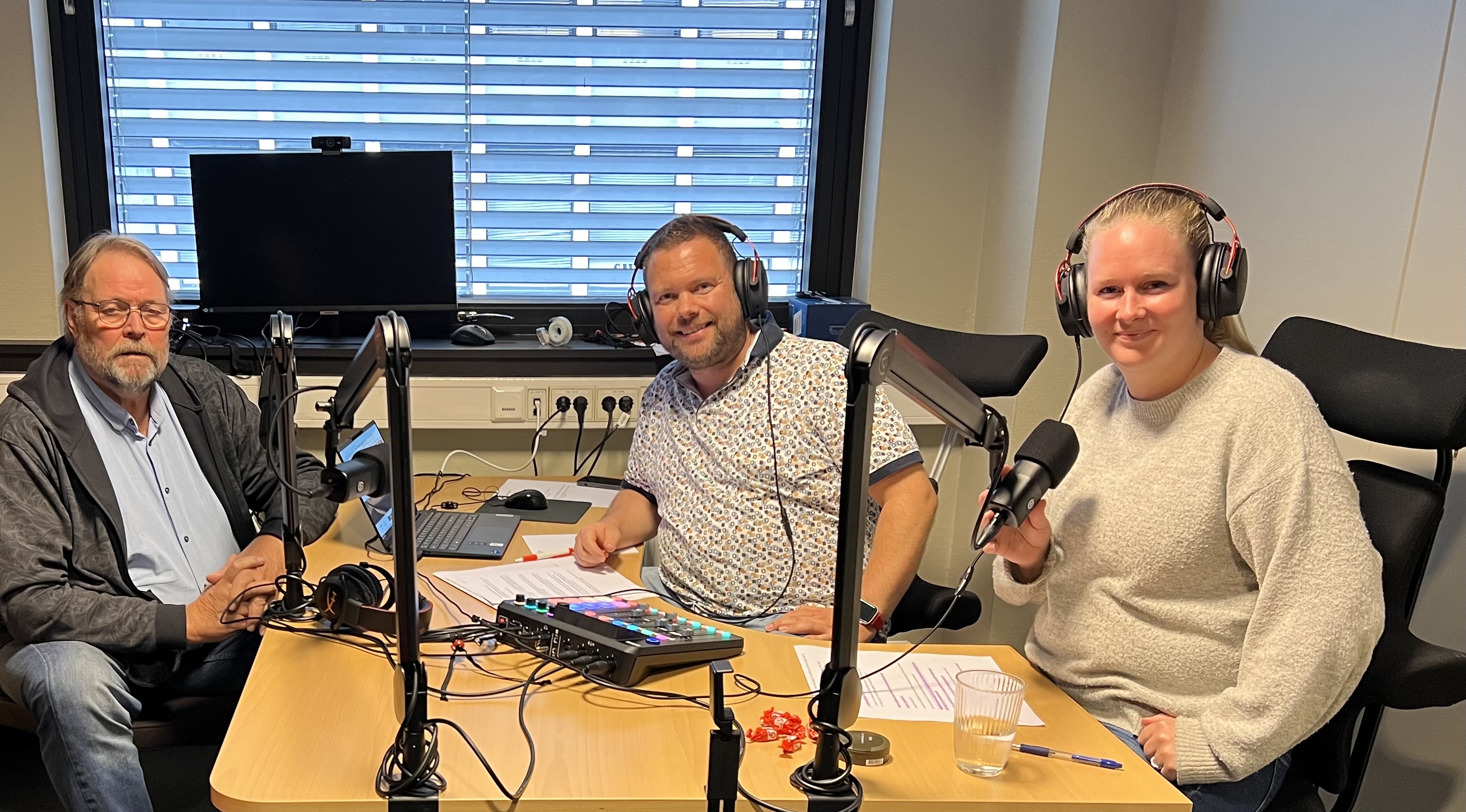 Johnny Skogsrød sitter til venstre i bilde av studio, videre sitter Ole-Henrik Olsen og Christine Rise som er programledere.