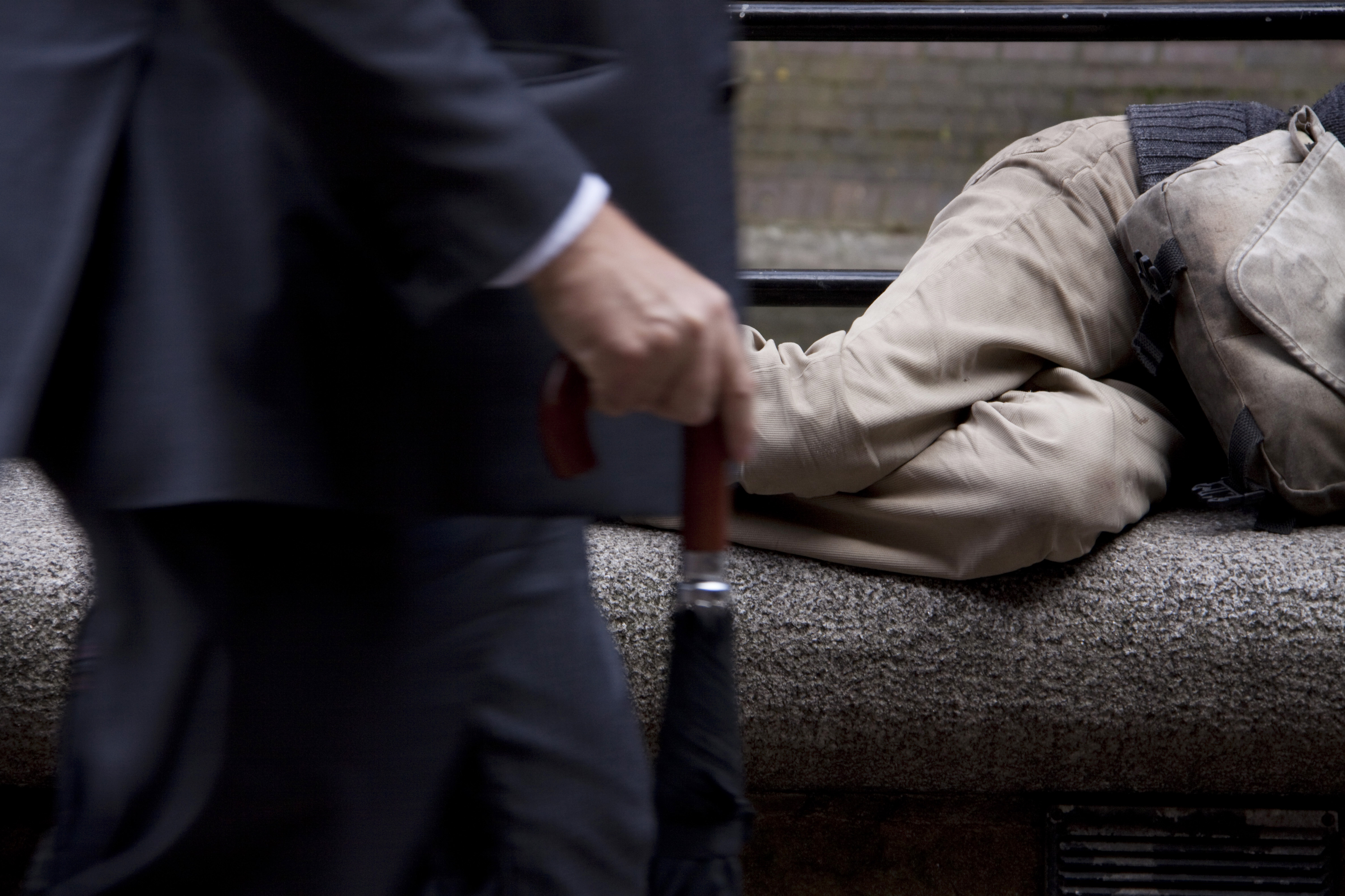 En fattig person ligger på en benk, en velstående mann i dress går forbi