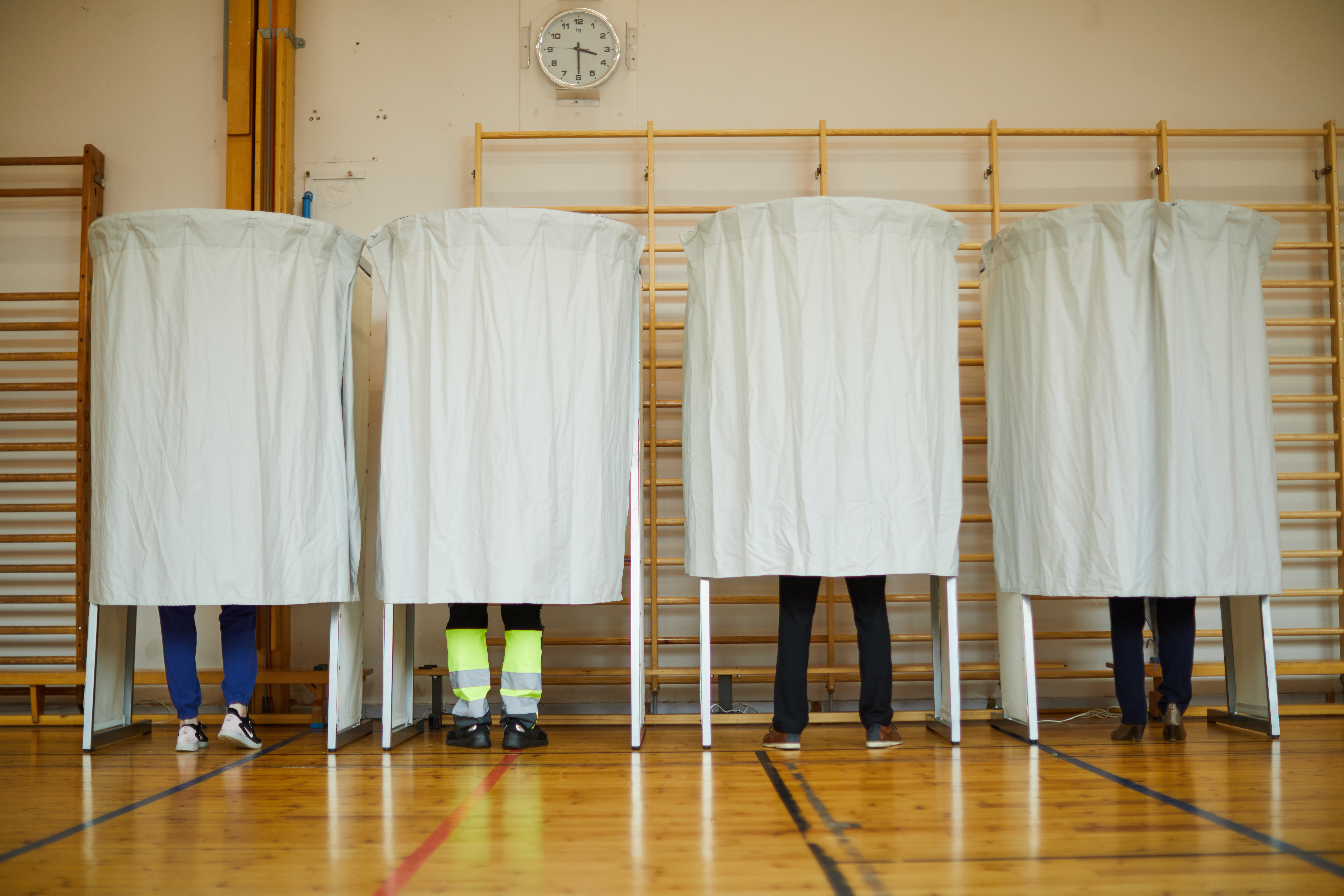 Stemmeavlukker hvor man kun ser fire par ben som står innenfor avlukkene. Illustrerer demokrati og valg.