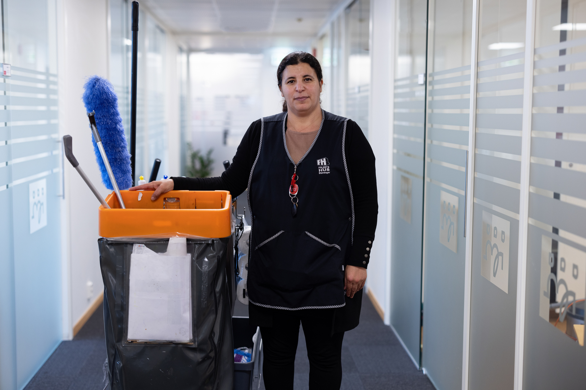 Kvinnelig renholder som står ved siden av vasketralle. Foto.