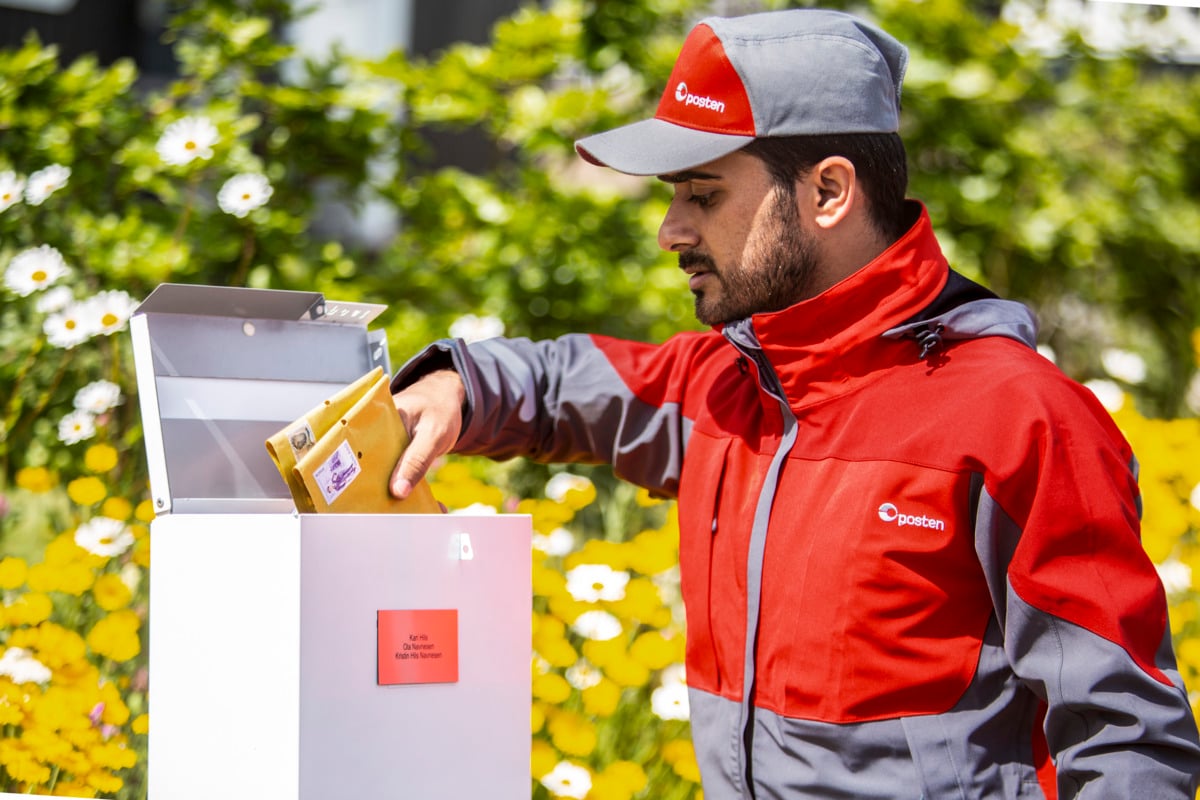 Postmann i uniform legger to brev i en postkasse. Foto.