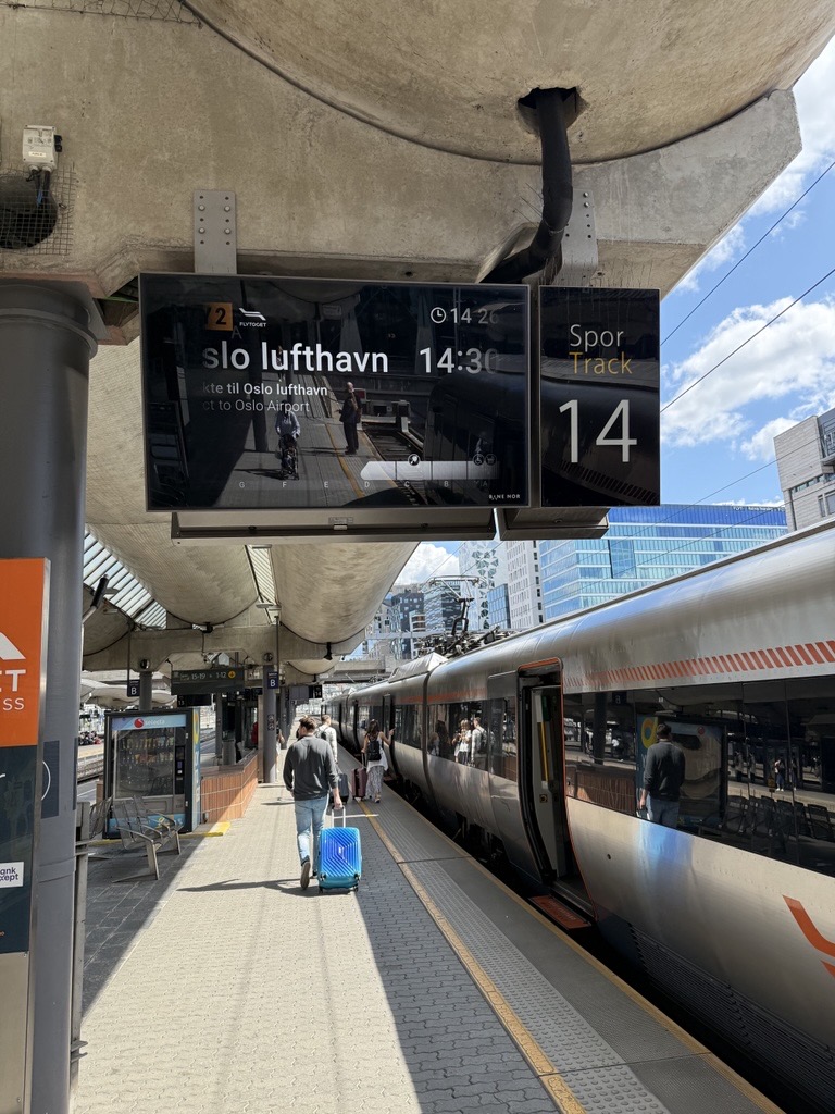 skjerm som viser avgangen til flytoget ute på perrong ved siden av flytoget