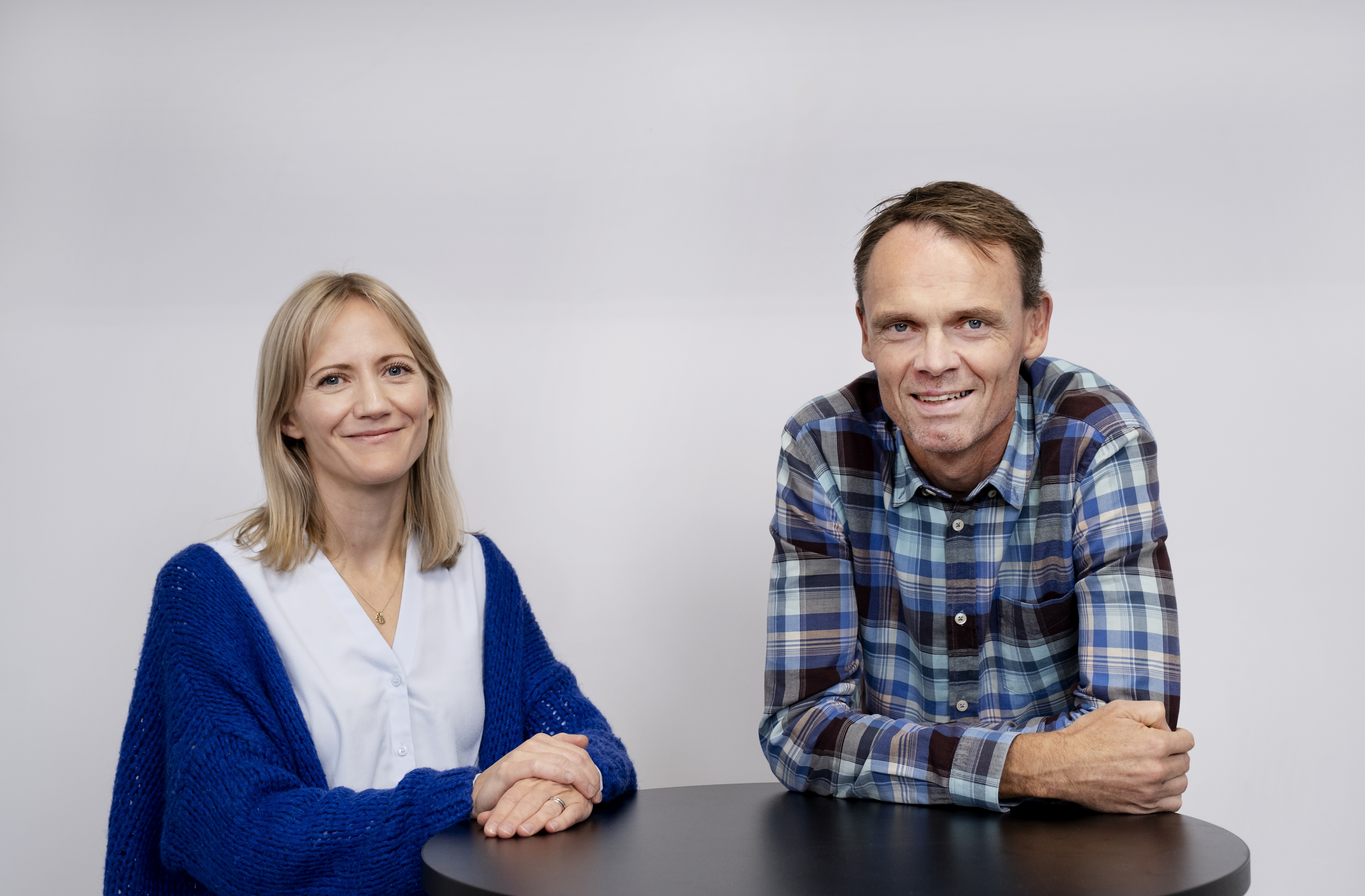 En kvinne og en mann som lener seg på armene over et høyt bord. Foto.