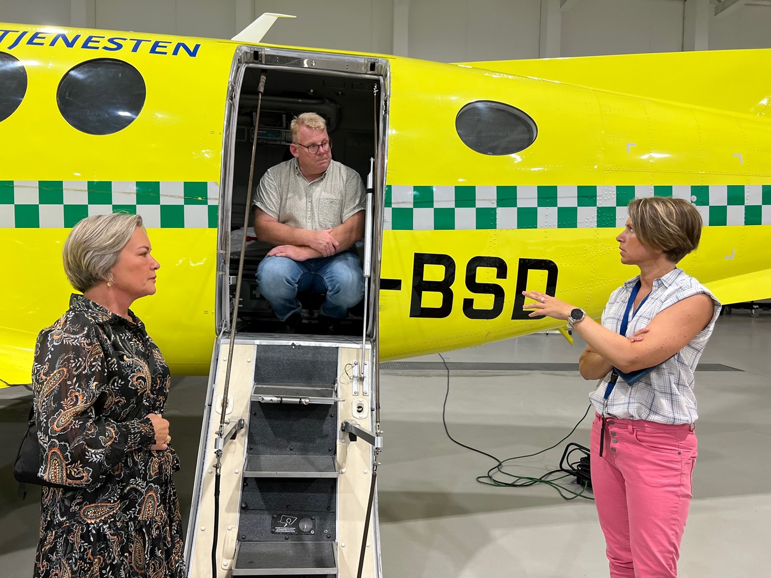 Tre mennesker foran en luftambulanse. Foto.