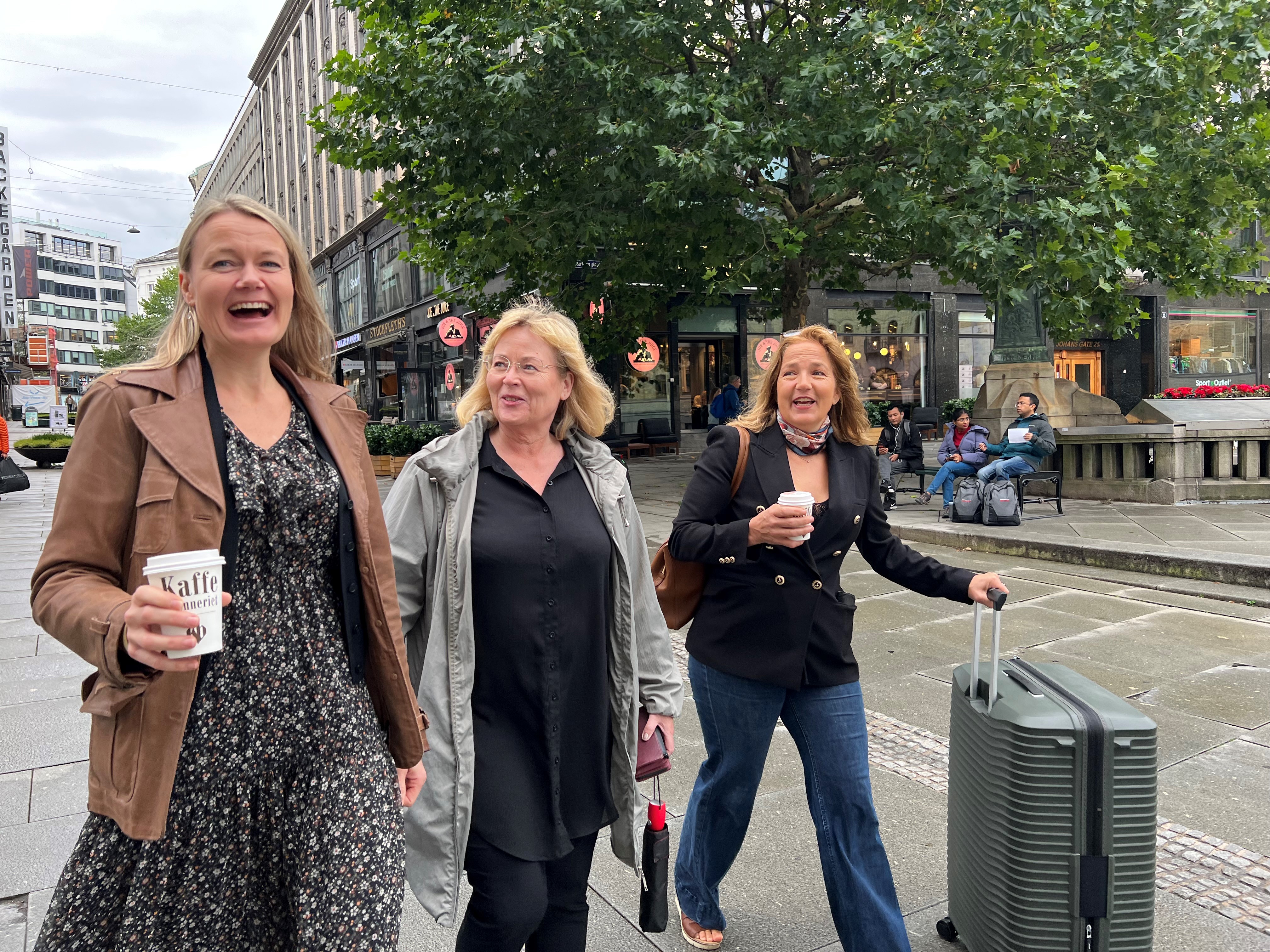 Tre kvinner går smilende ned en gate. Foto.