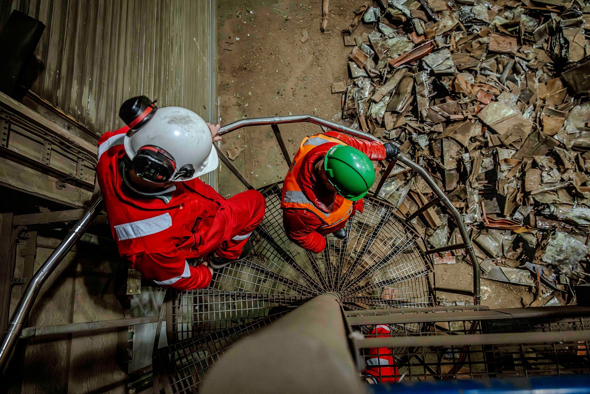 To personer i arbeidstøy og vernehjelm går ned en vindeltrapp. Foto.