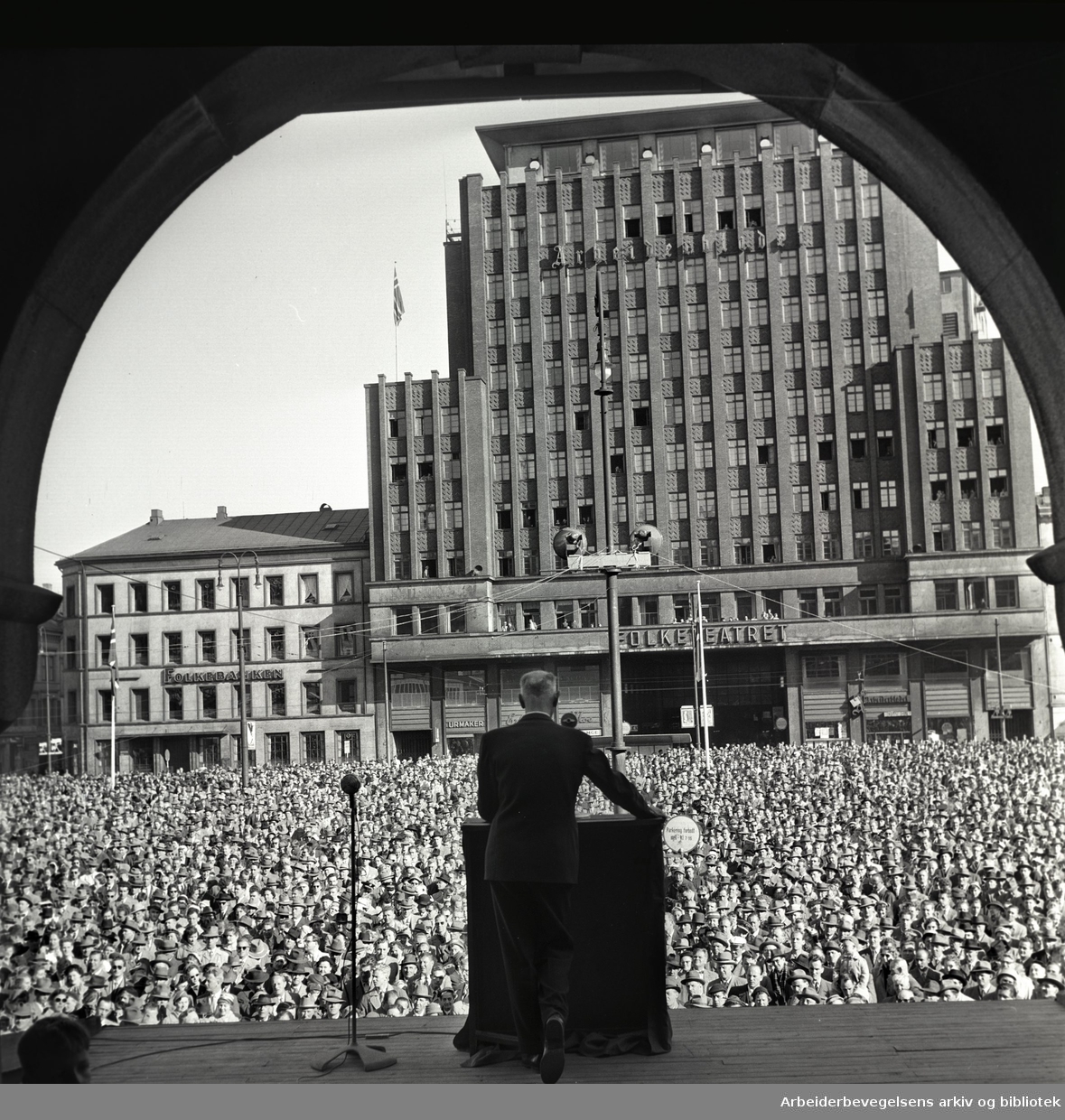 Bilde av Einar Gerhardsen som holder tale.  Bildet er tatt bakfra og du ser den store folkemengden på Youngstorget.