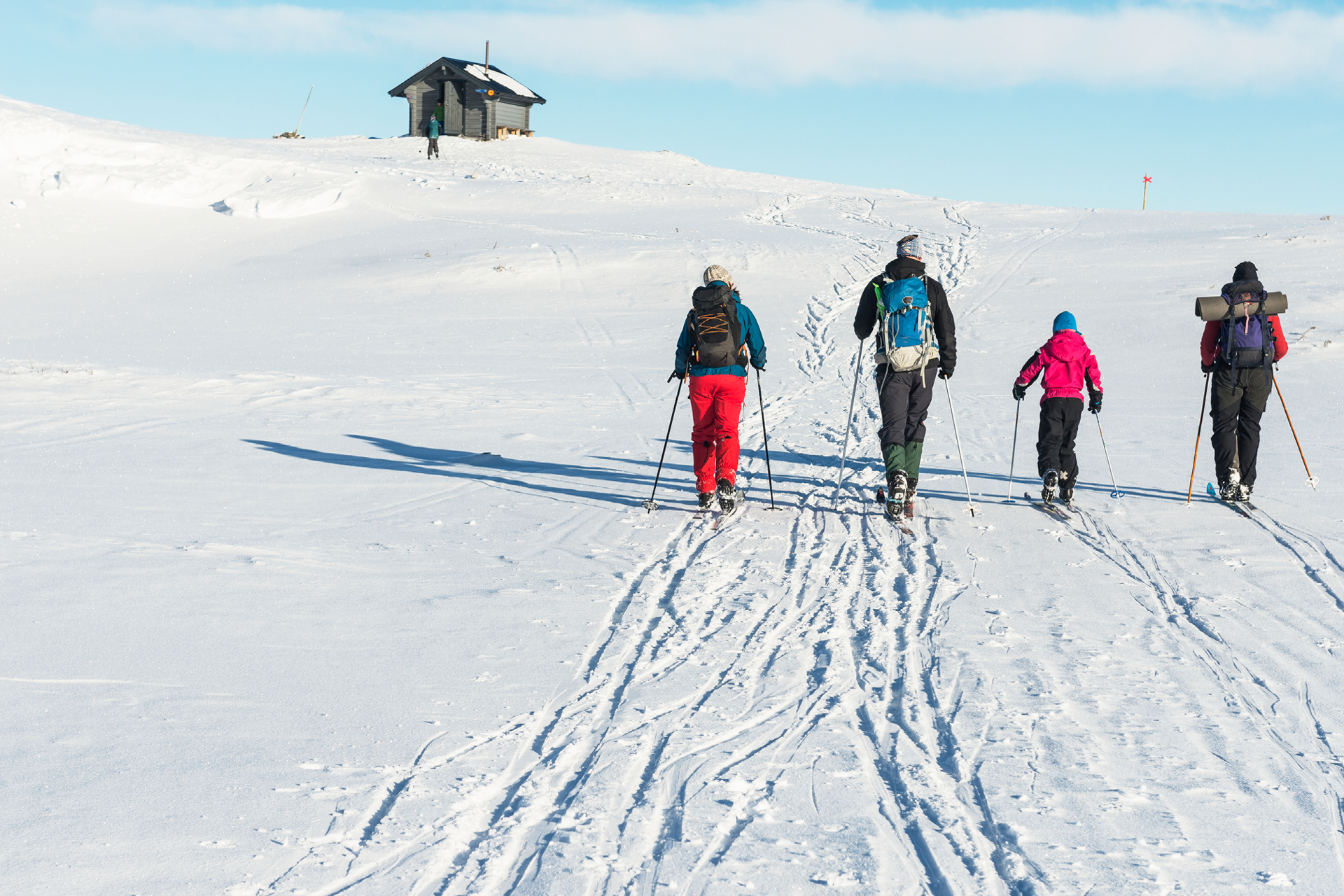 Folk går på ski innover mot en hytte i det fjerne.