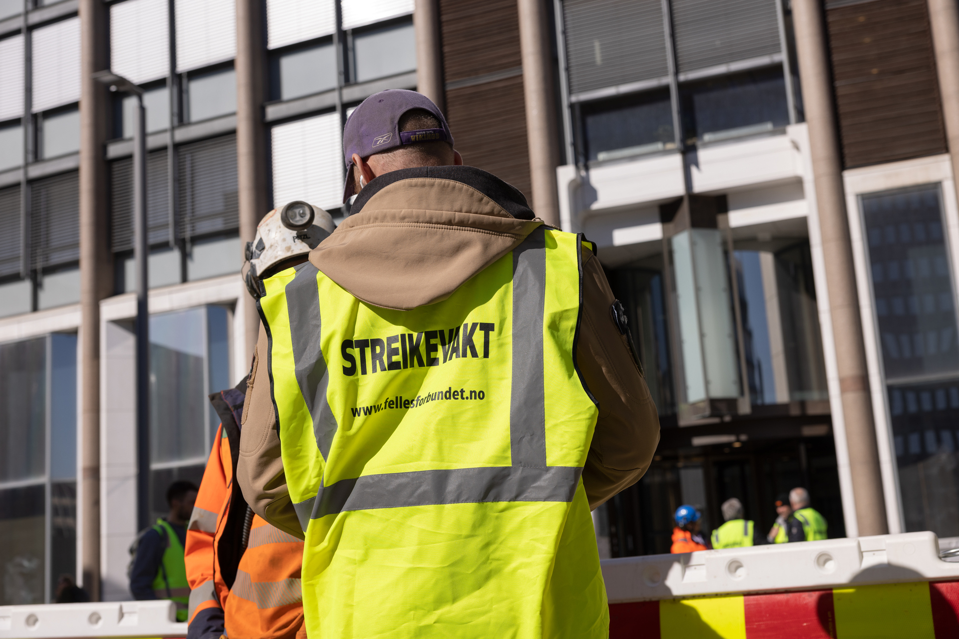 Mann i streikevest står med ryggen til foran et bygg ute. Foto