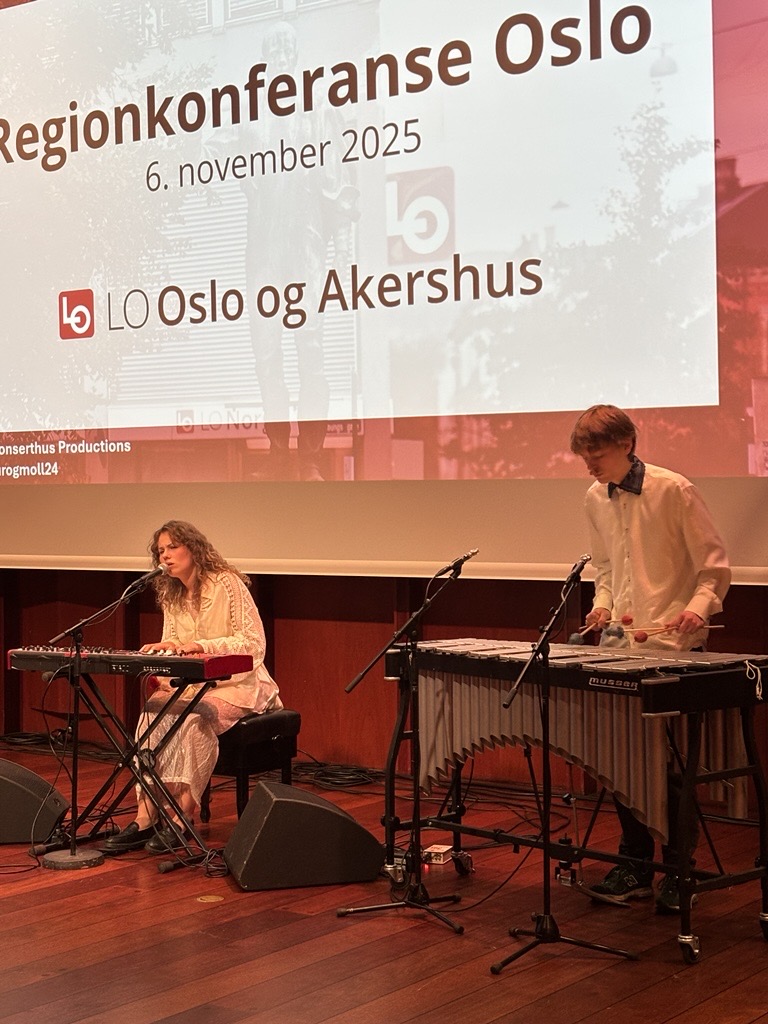 en kvinne på piano synger med en mann på et lite slaginstrument