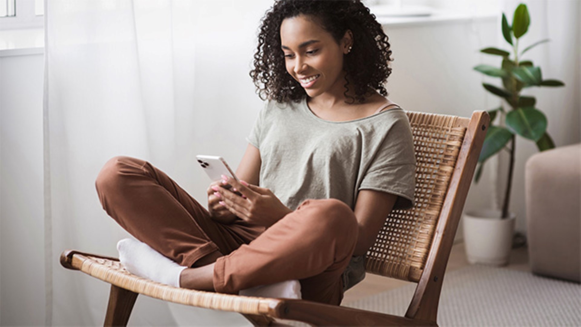 Kvinne sitter i stol og ser på mobiltelefon. Foto.