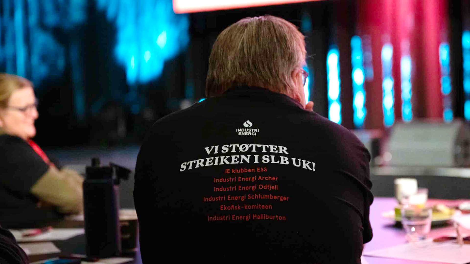 En person sitter med ryggen til og viser genser med streiketekst på. Foto.