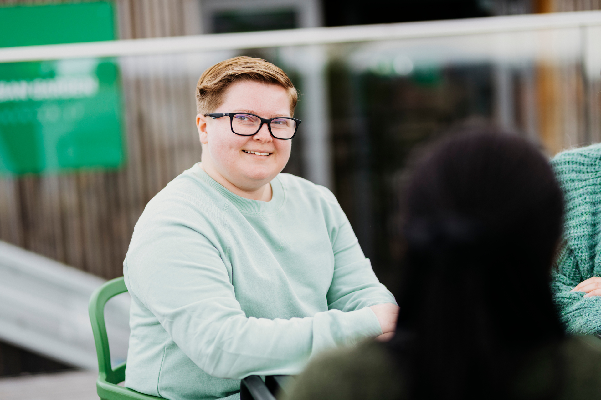 ung person sitter ute og ser mot kamera. Foto.