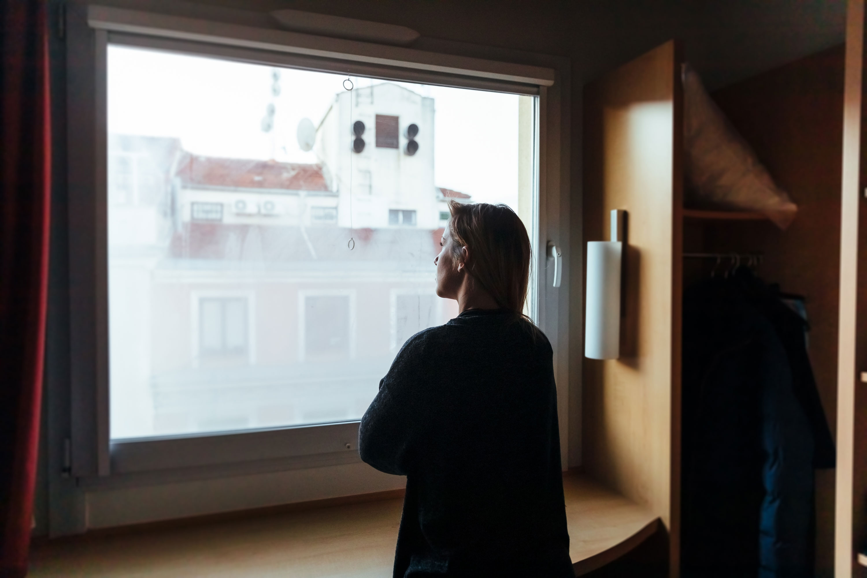 Kvinne ser ut av vinduet fra en leilighet. Foto.