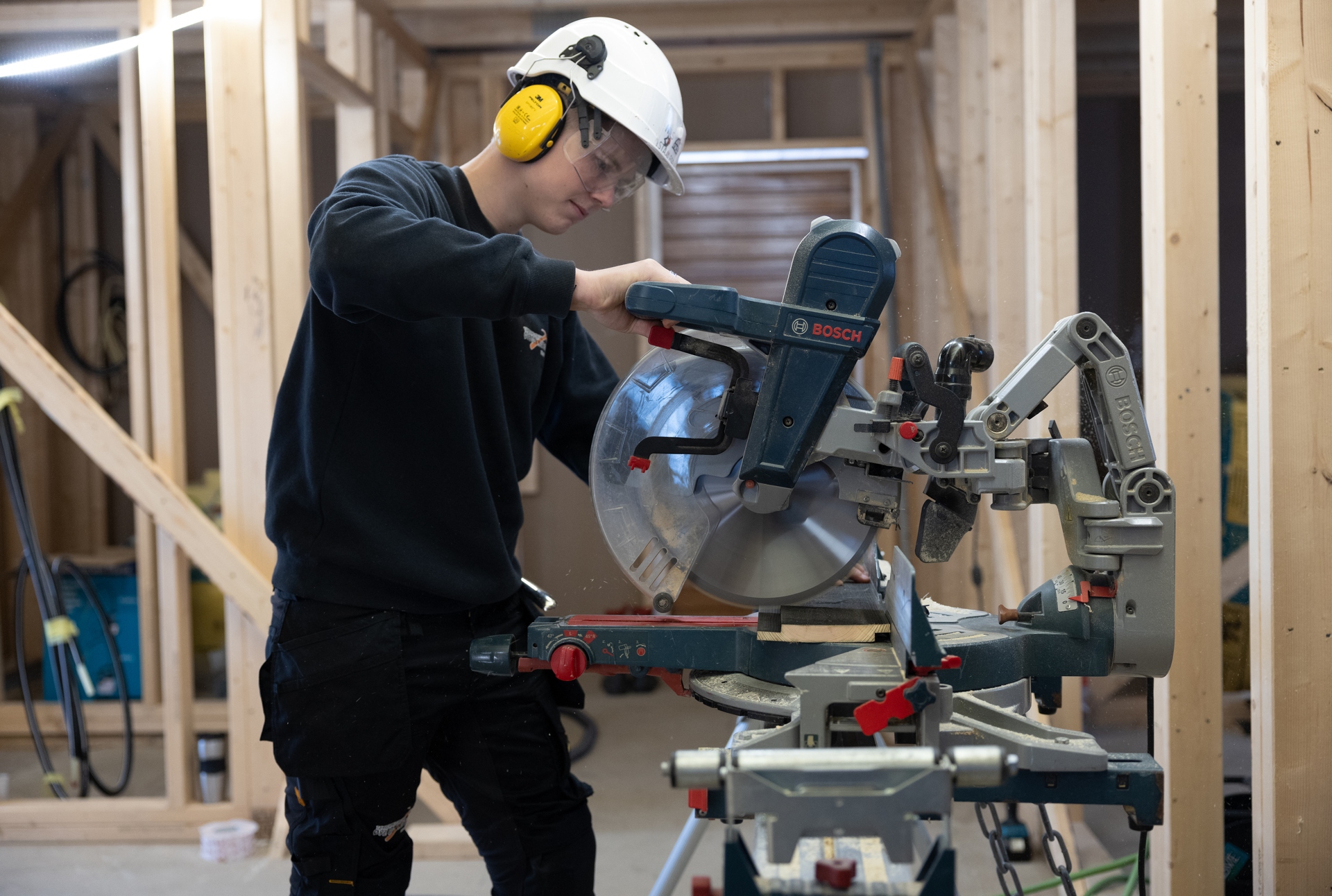 Ung tømrer som jobber med kapp- og jærsag på en byggeplass. Foto.