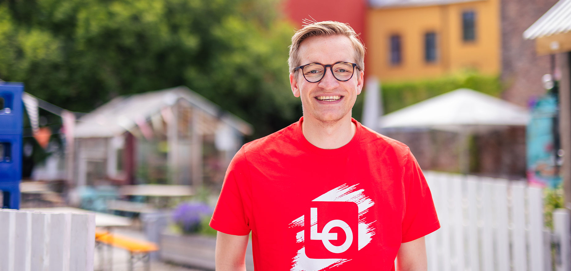 Ung mann i rød t-skjorte står utendørs og smiler.