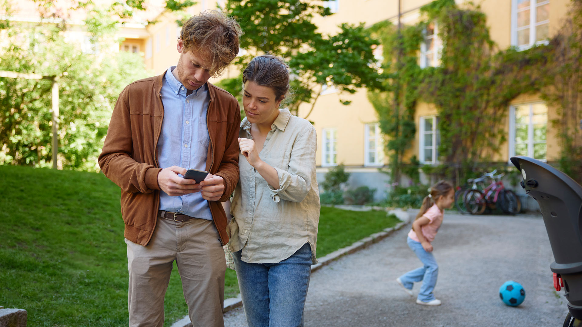 Ung mann og kvinne står sammen ute og ser på en mobiltelefon. Foto.