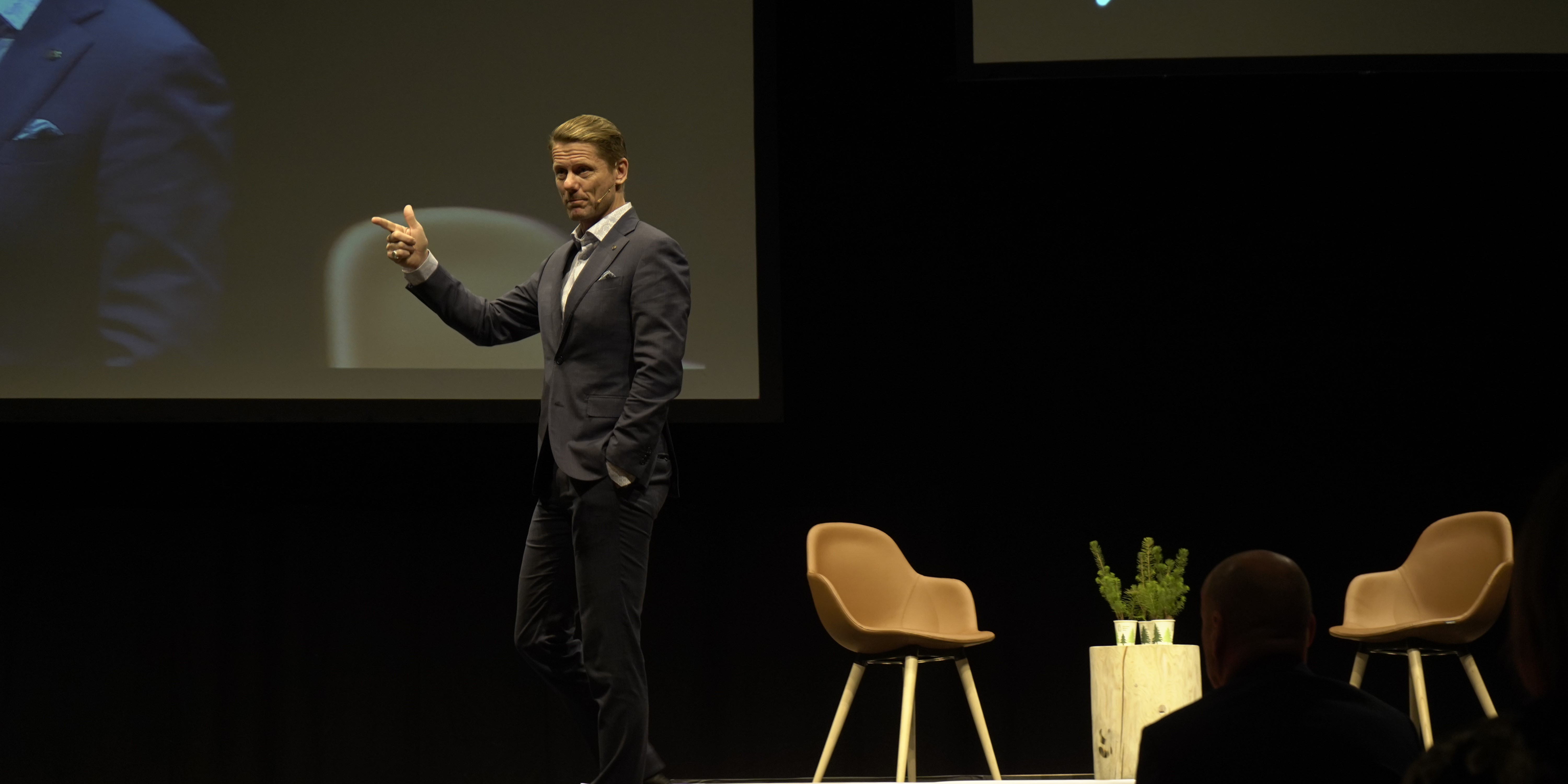 Kjetil Staalesen pekende framover på vei over scenen. Sorskjerm i bakgrunnen