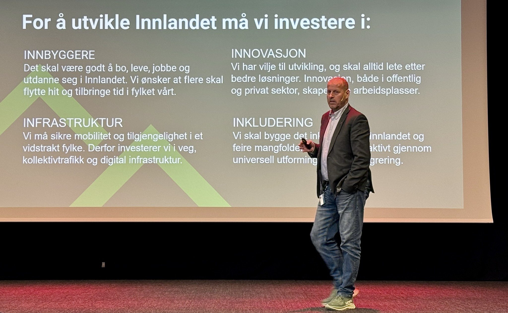 Thomas Breen på scenen foran et 4-punktsbilde fra fylkeskommunens politiske prioriteringer for vekst i Innlandet