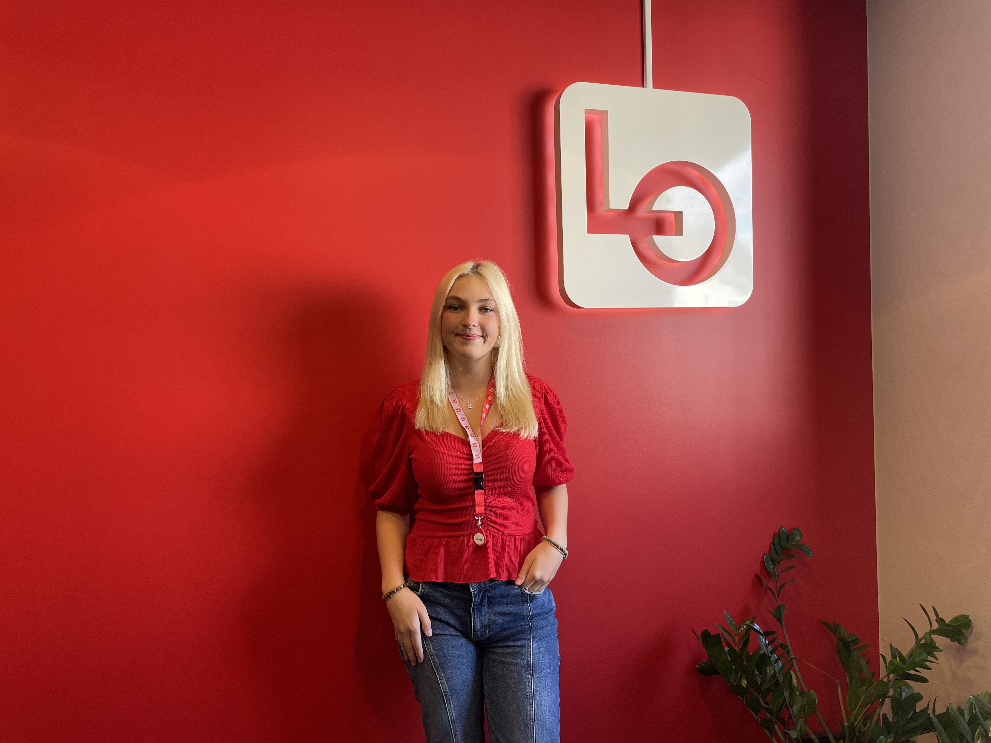 Vår nye lærling Levina i bildet, foran en rød vegg med LO-logo.