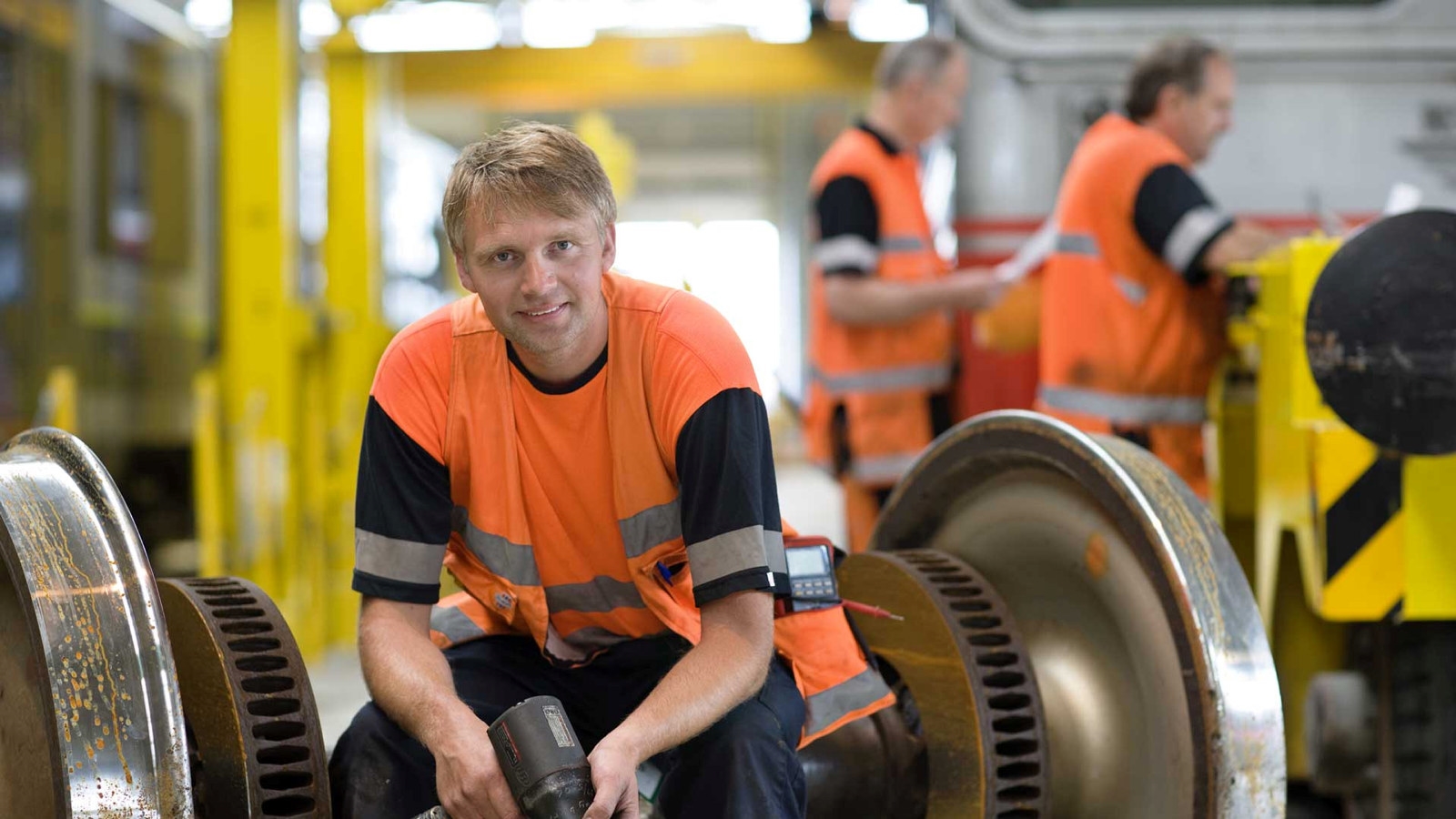 Ung mann i arbeidsklær sitter og smiler til kamera. Foto.