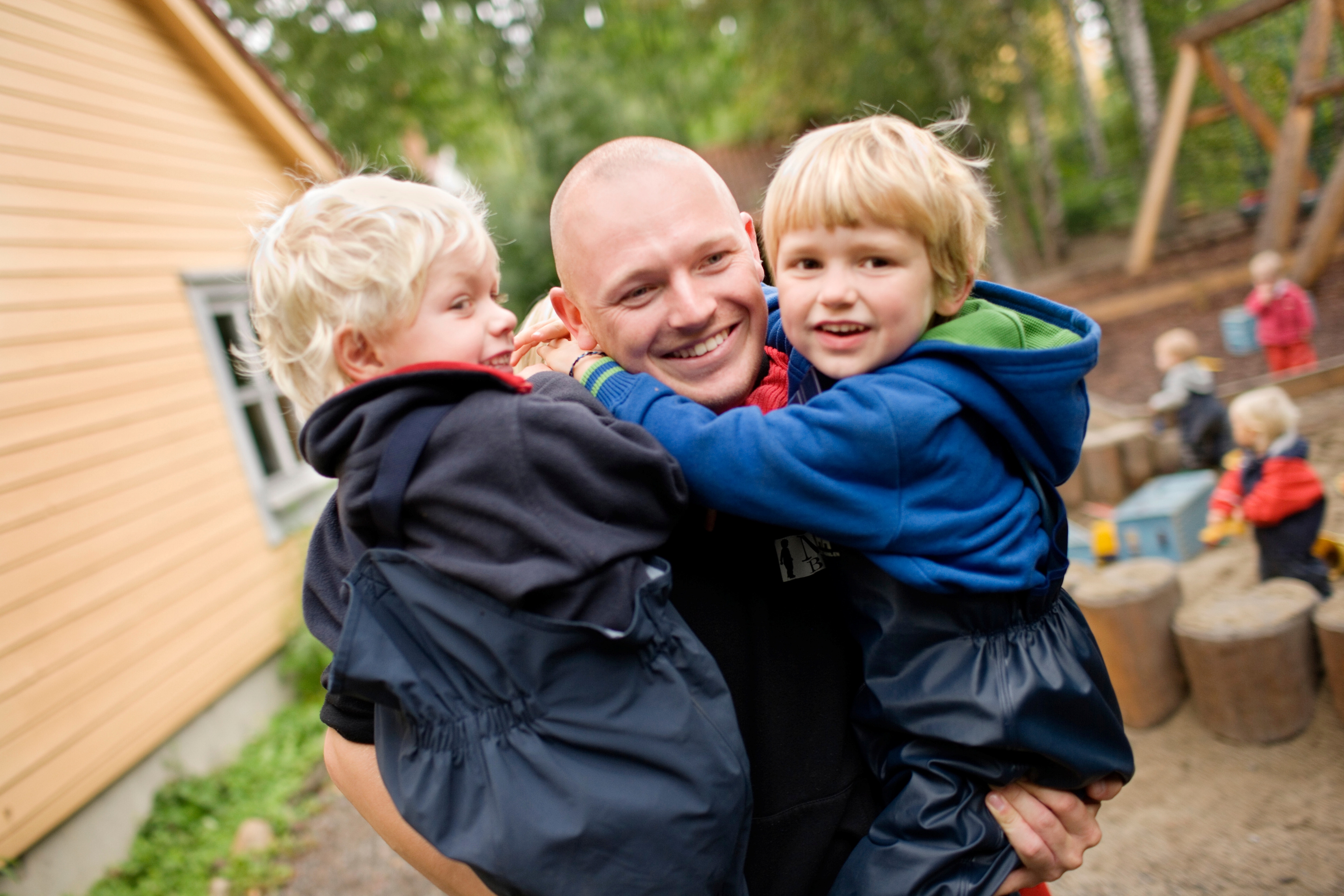 Voksen mann som bærer to små barn på hver sin arm. Foto.
