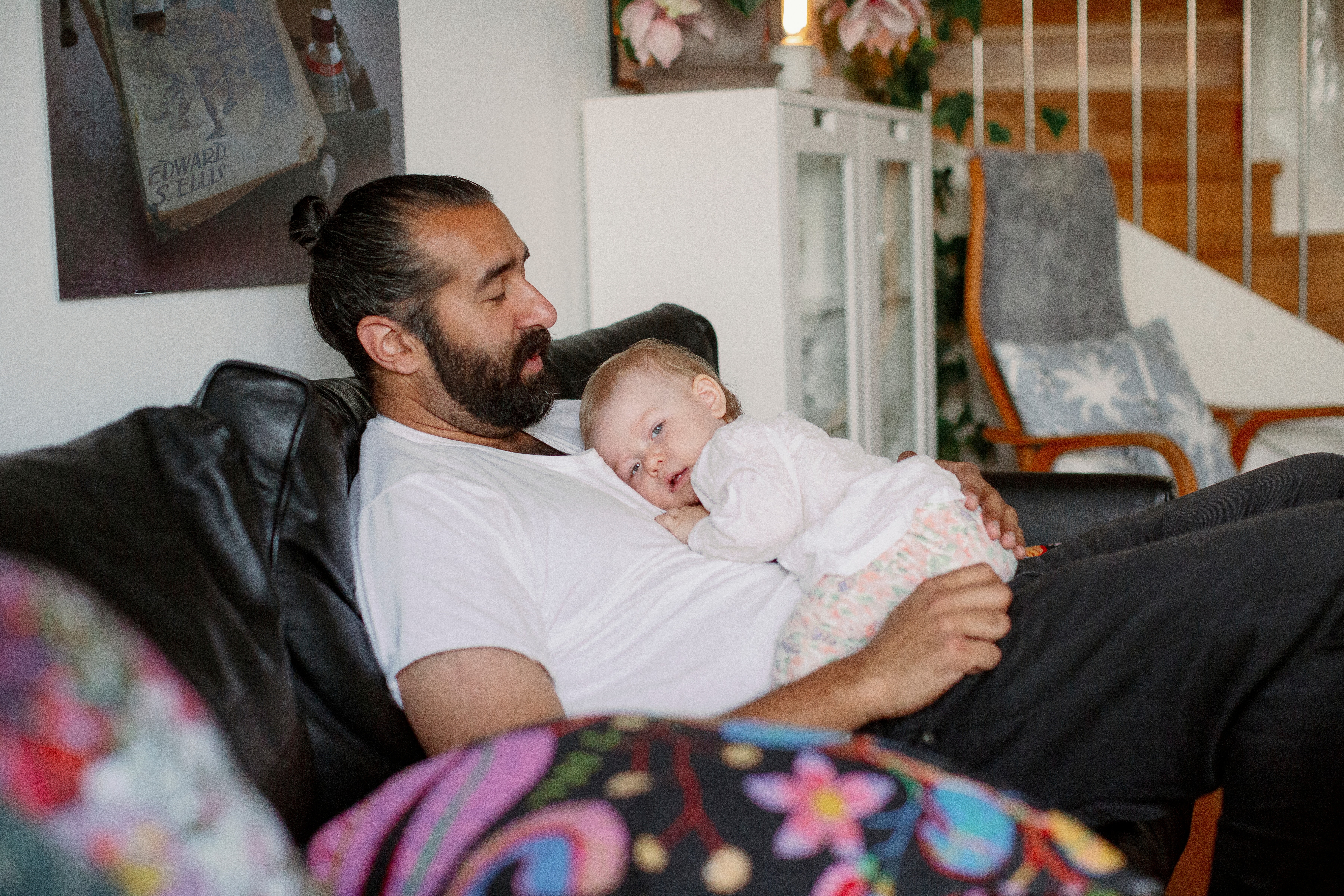 Far med liten datter på fanget sitter i sofaen. Foto.