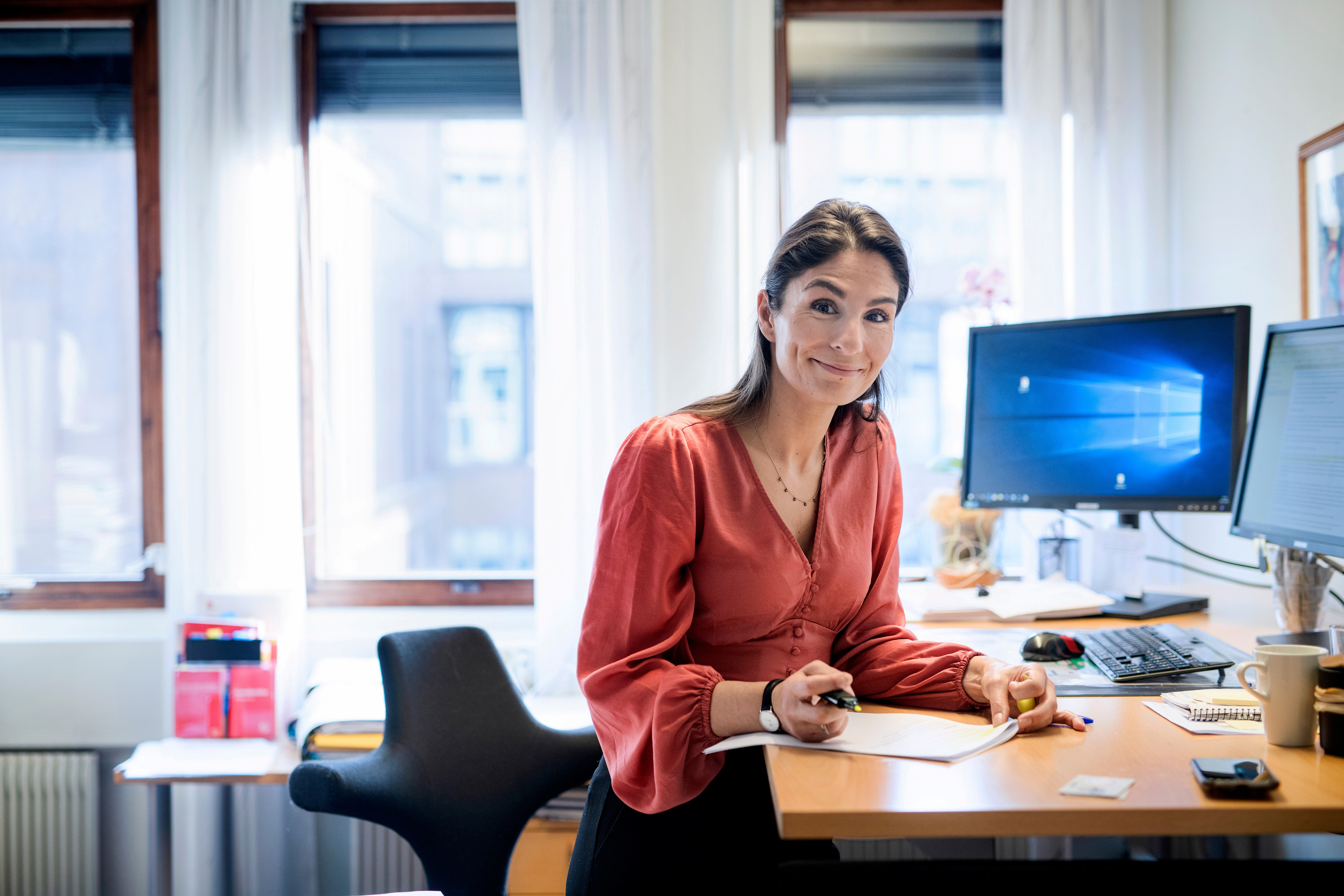 Kvinnelig arbeidstaker sitter ved kontorpulten sin og sr mot kamera. Foto.