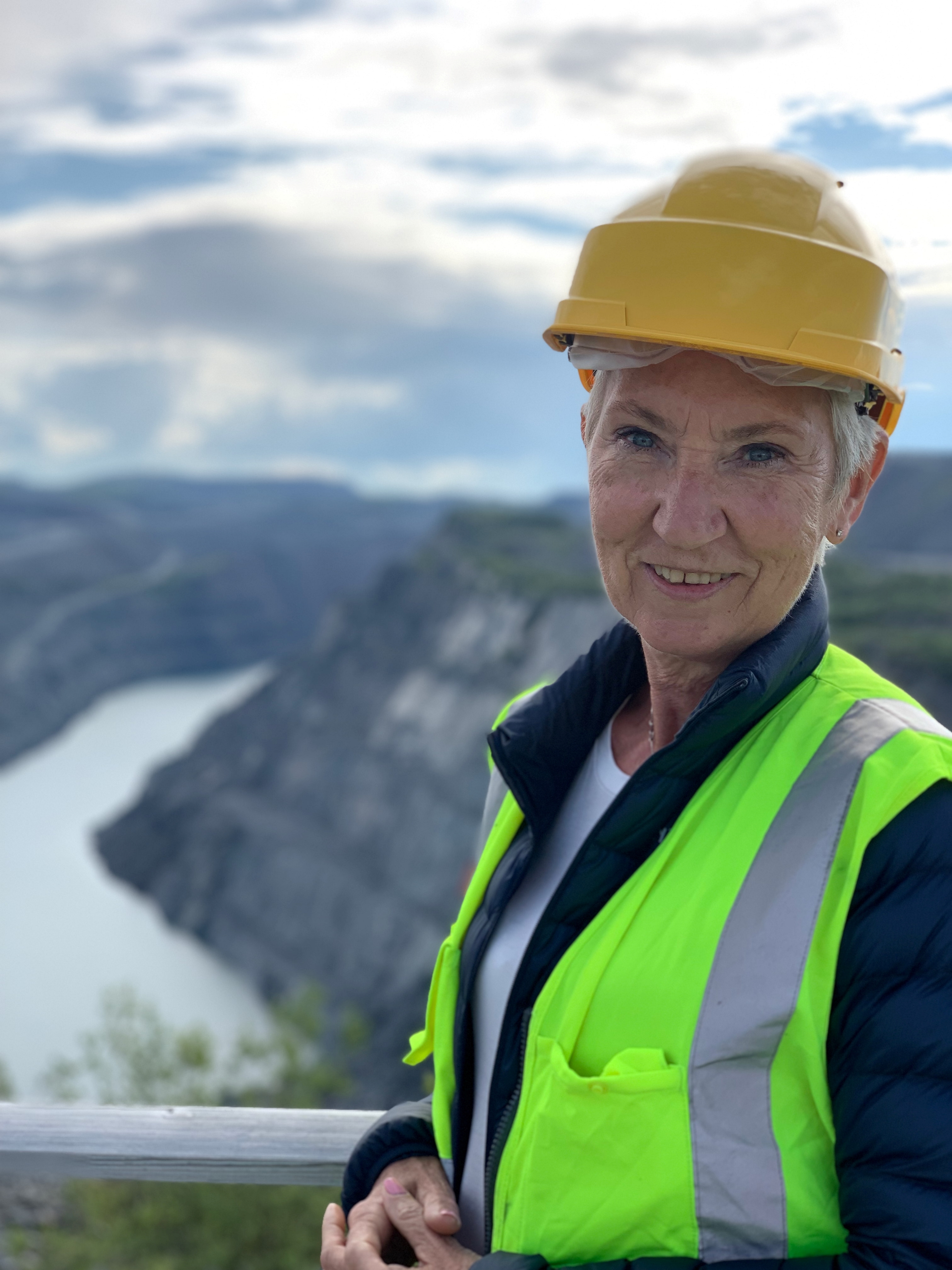 LO-leder Peggy Hessen Følsvik i gul arbeidsvest og gul vernehjelm med utsikt over fjord. Foto.