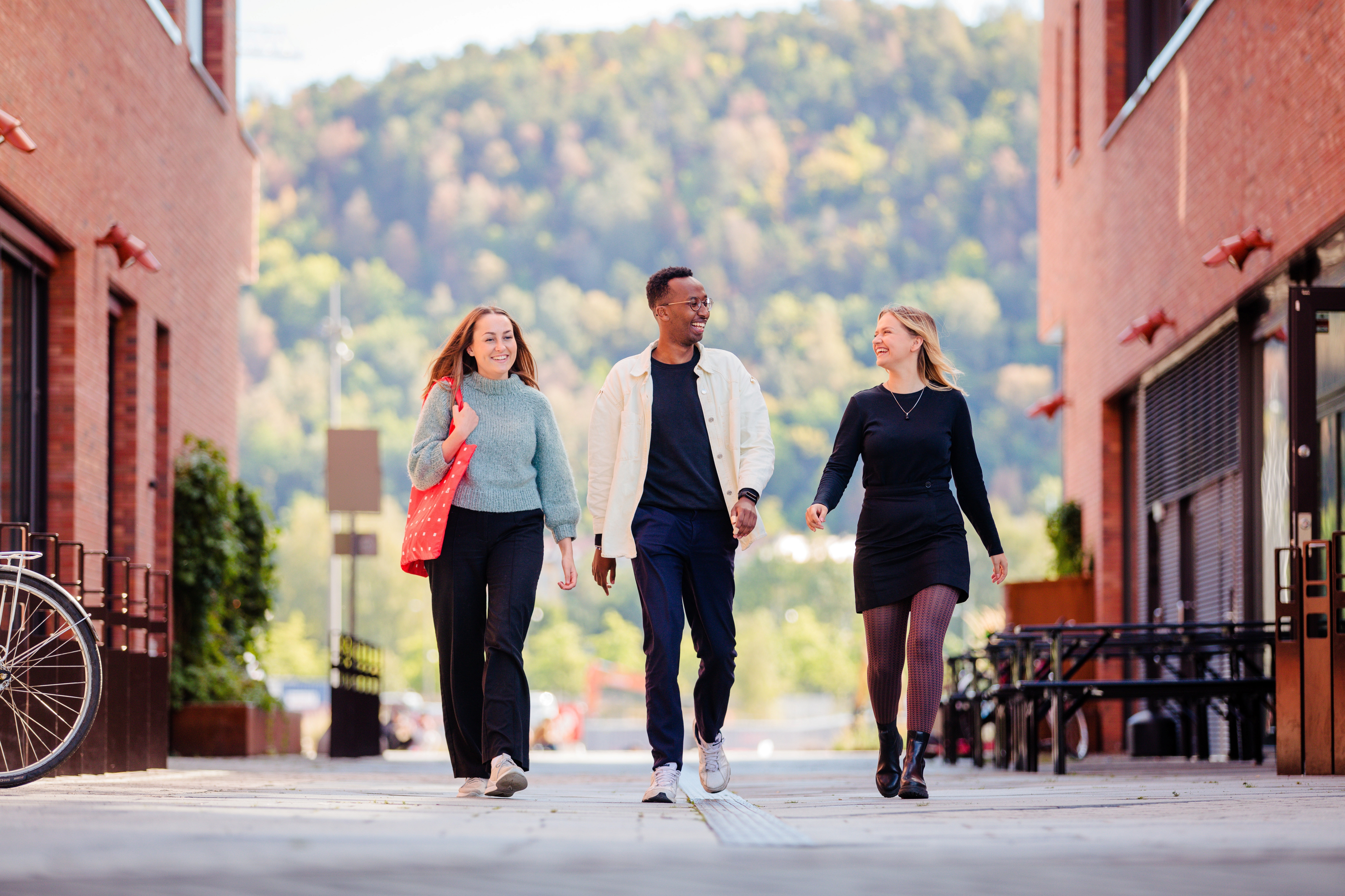 Tre studenter går sammen ute og smiler. Foto.