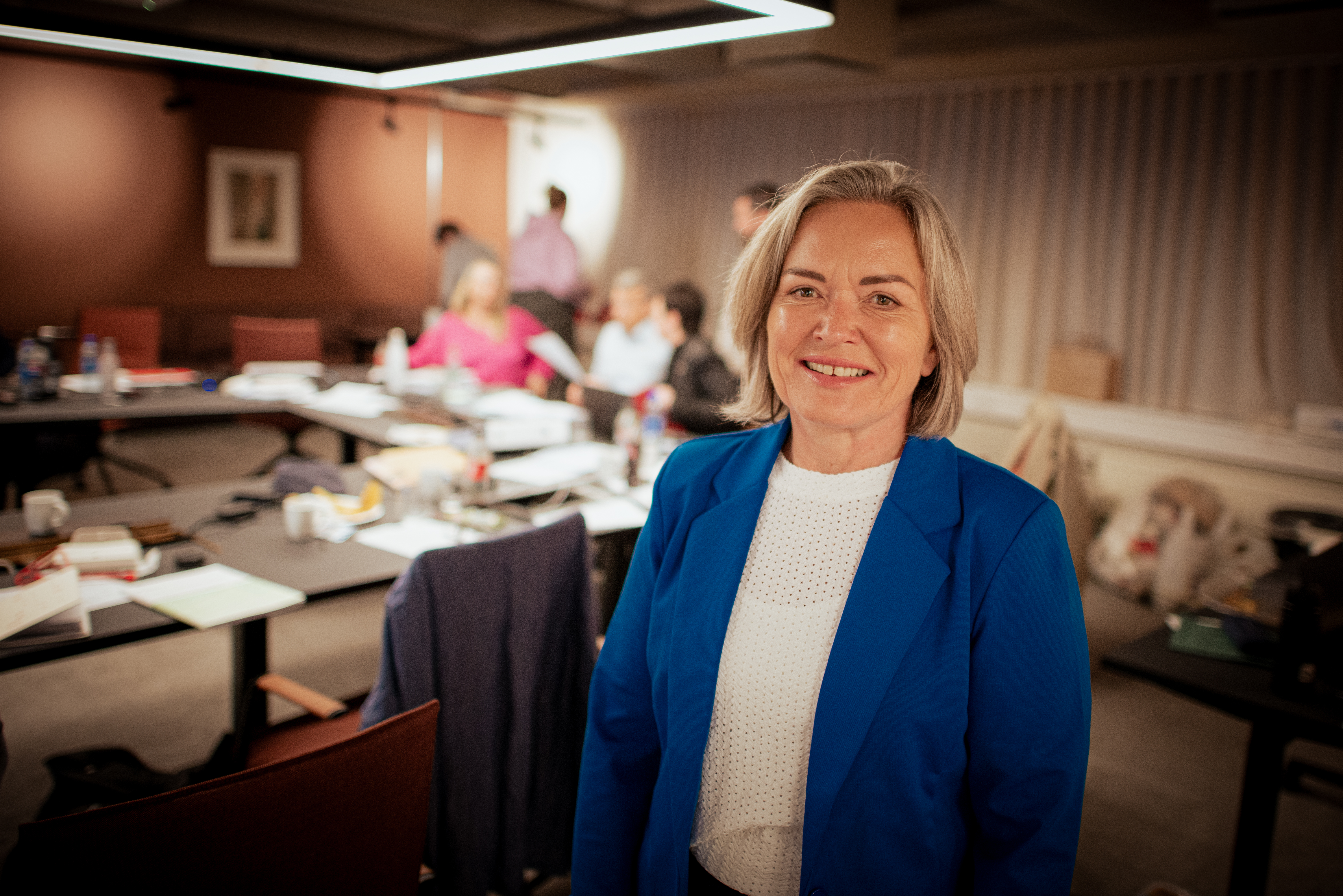 LOs nestleder Sissel Skoghaug ser i kamera. Rom med mennesker i bakgrunn. Foto.