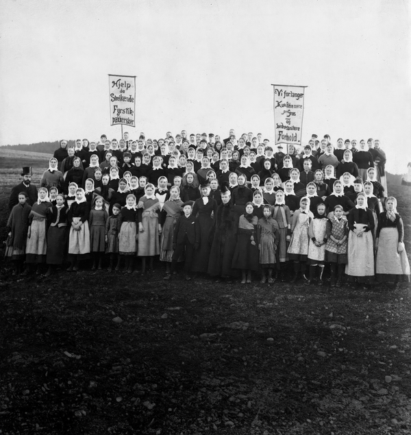 Bildet viser streikende fyrstikkarbeidere på Bryn fyrstikkfabrikk i 1889. De står i samlet flokk med fagforeningsbannere og ser intenst inn i kamera. Nesten alle er kvinner. 